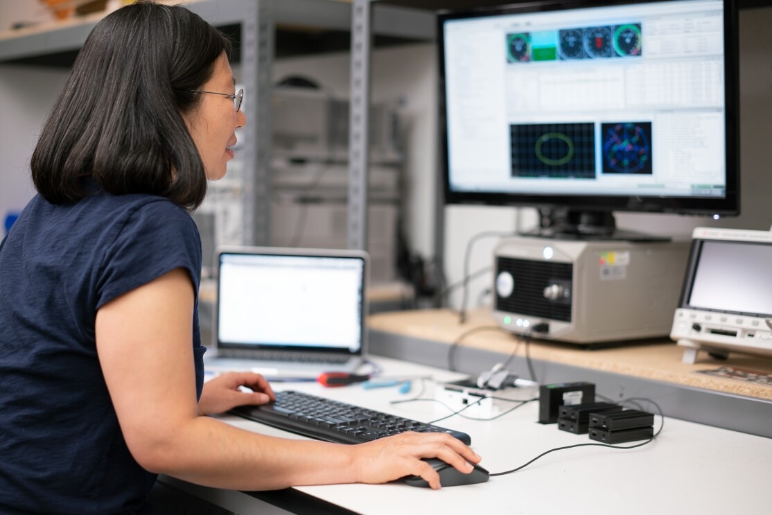 A woman works on a computer, one hand on the keyboard, the other on a mouse, while she looks at diagrams on a screen. 