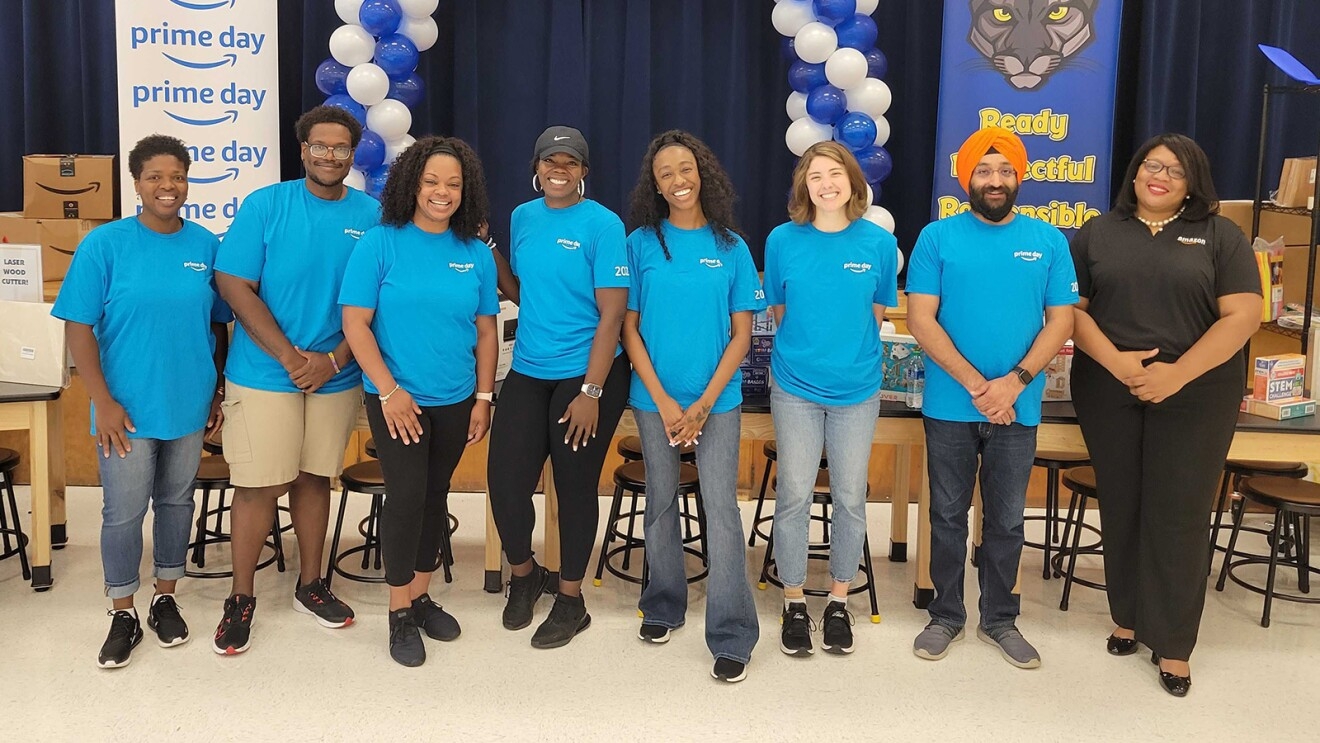 A group of volunteers wear blue T-shirts and stand in front of a blue and white balloon arch.