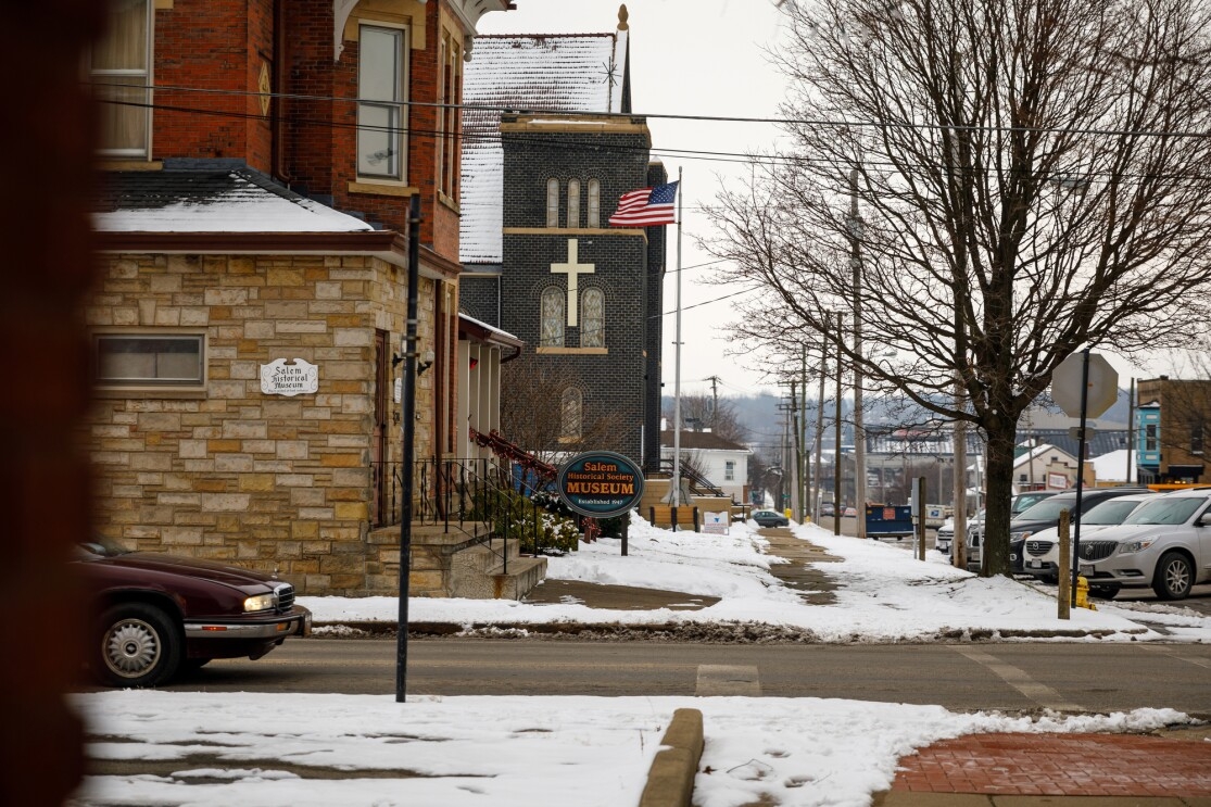 An church and an American flag are at the center of the image. A sign in front of a stone building reads "Salem Historical Society Museum."