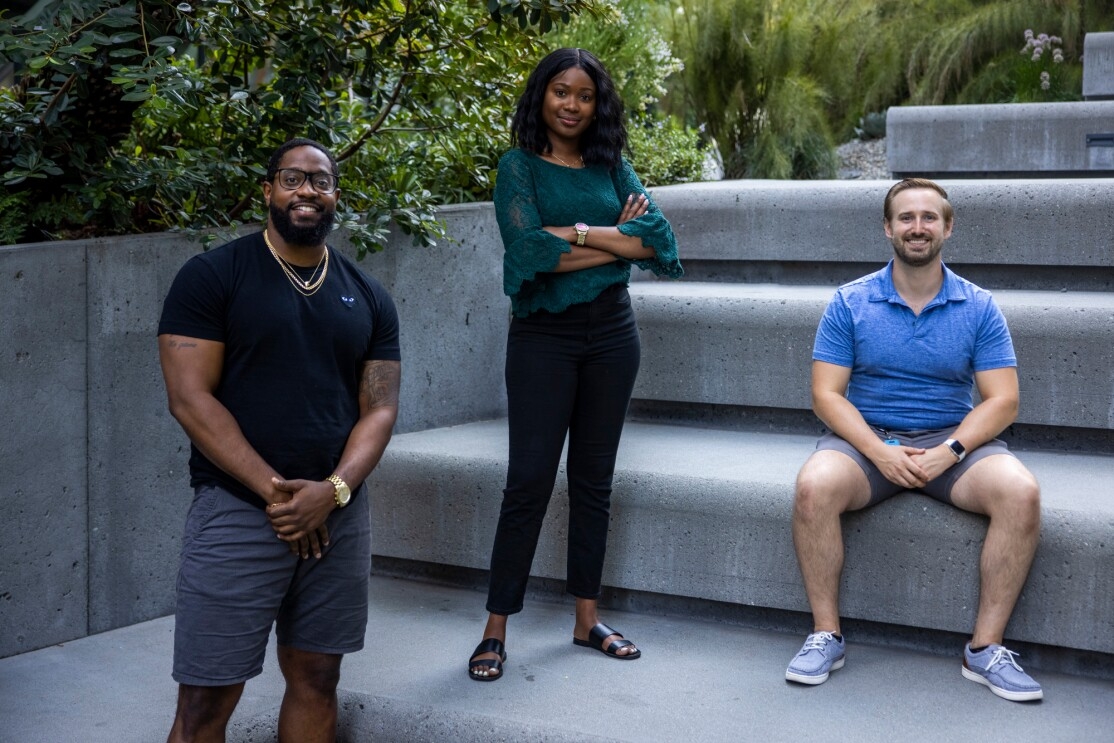 A woman and two men photographed on a tiered concrete seating area.