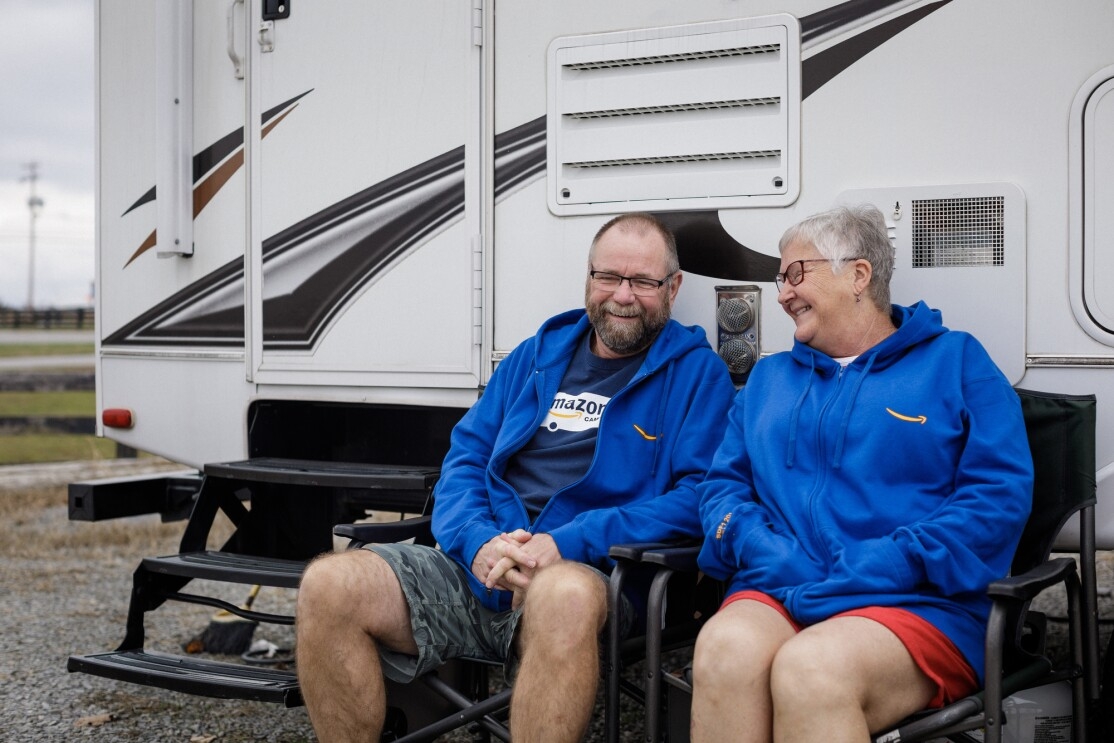 A man and woman sit together and laugh outside a RV.
