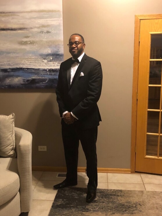 A man in a tuxedo stands in a living room.