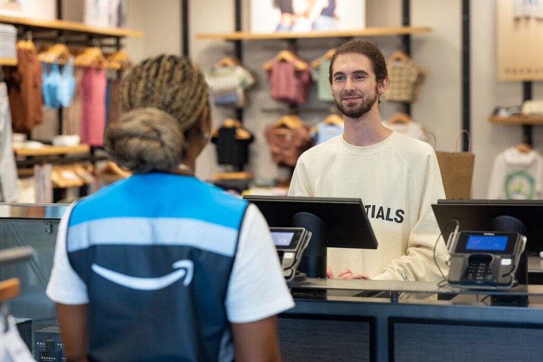 The process of an Amazon employee walking into a PacSun retailer, a PacSun employee putting items into retail bags, the Amazon employee talking with the PacSun employee, and the Amazon employee carrying the PacSun bag with the ordered items out of the store.
