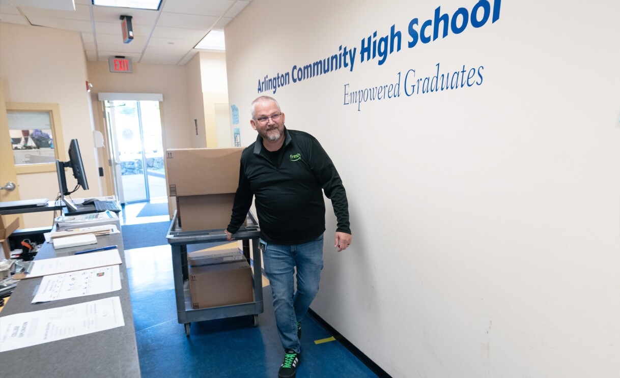 An image of a man with a cart full of boxes walking down the Arlington Community High School hallway.