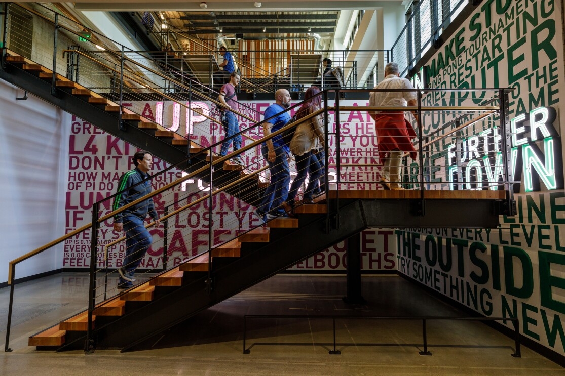 Amazon employees climb a set of stairs that are decorated with inspirational slogans, like "try something new".