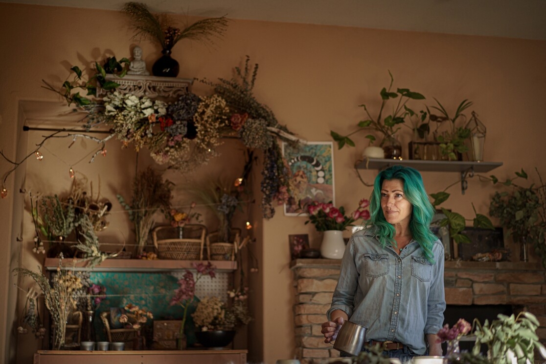 A woman wearing denim clothes stands in a room decorated with dried and living plants.