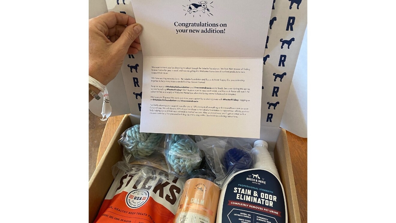 The Rocco & Roxie boxes the new puppy parents received when adopting their  dog is filled with jerky sticks, a calming supplement, toys and a stain and odor eliminator. There is also a note that reads at the top, "Congratulations on your new addition!" with a picture of a dog.