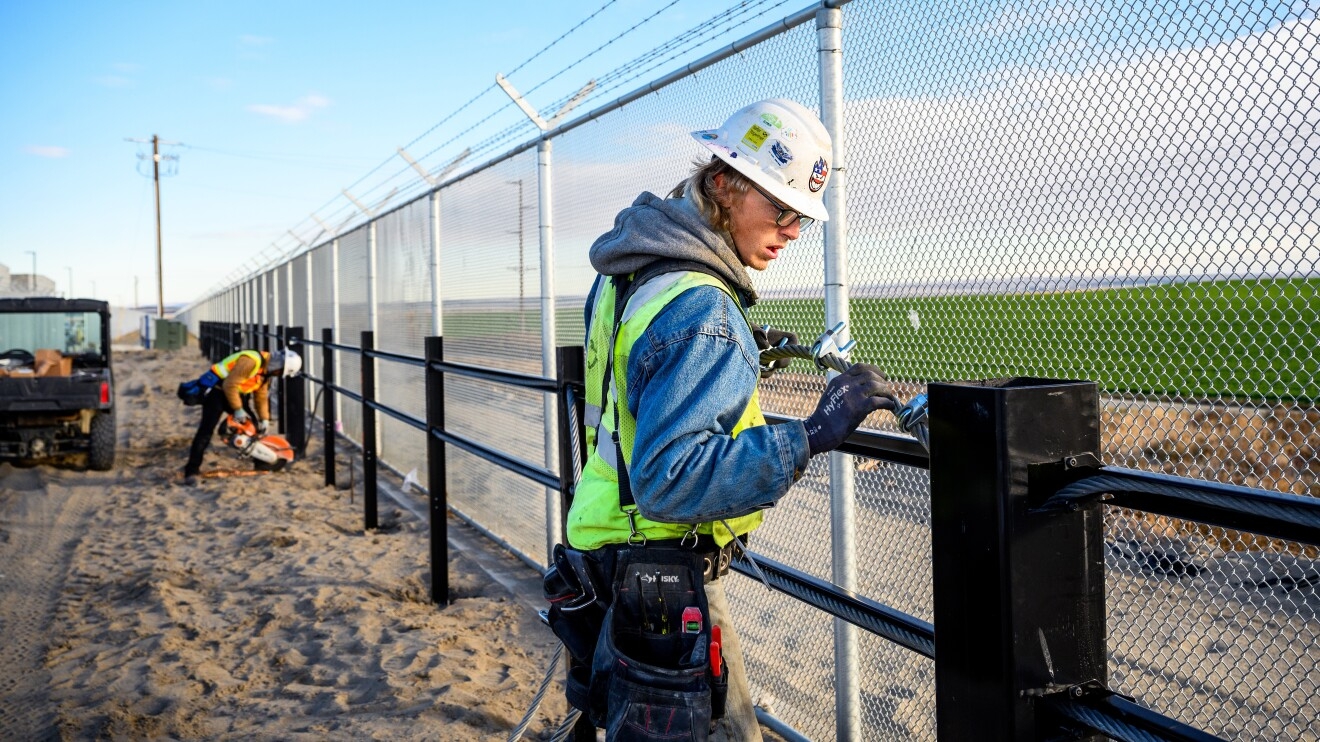 A photo of a construction worker building a high security fence at the property of an AWS data center.