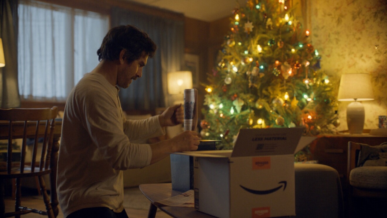 A man shreds newspaper in his living room with a lit Christmas tree in the background.