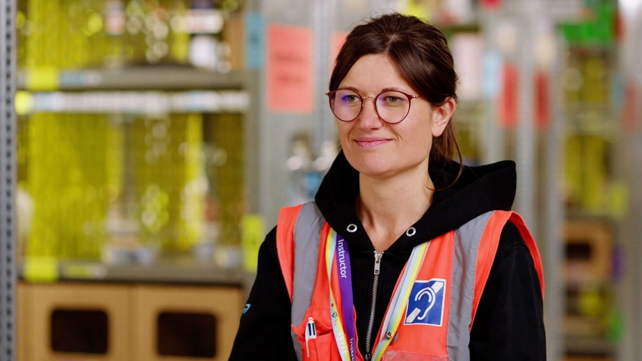 A photo of an employee who is hard of hearing at an operations facility. The employee is wearing a safety vest that displays a hearing impaired symbol.