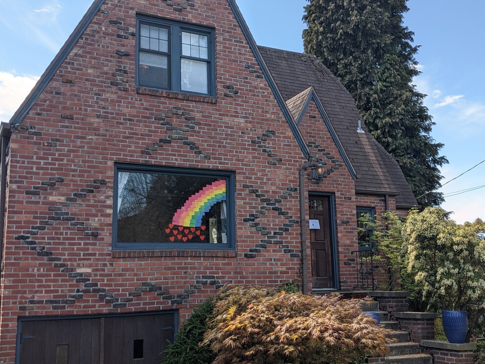Rainbow in the front window of a brick Tudor-style home during COVID-19 pandemic.