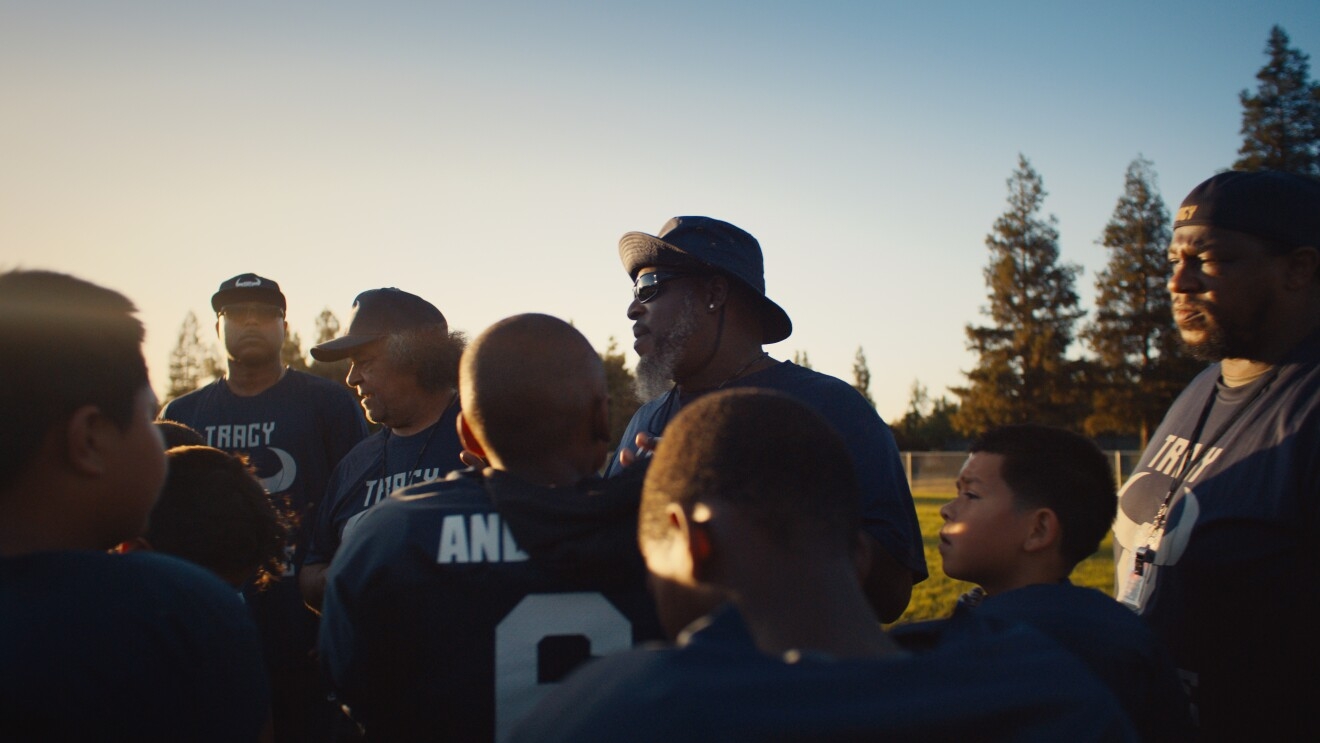 An image four adult football coaches standing in front of players on their little league team.