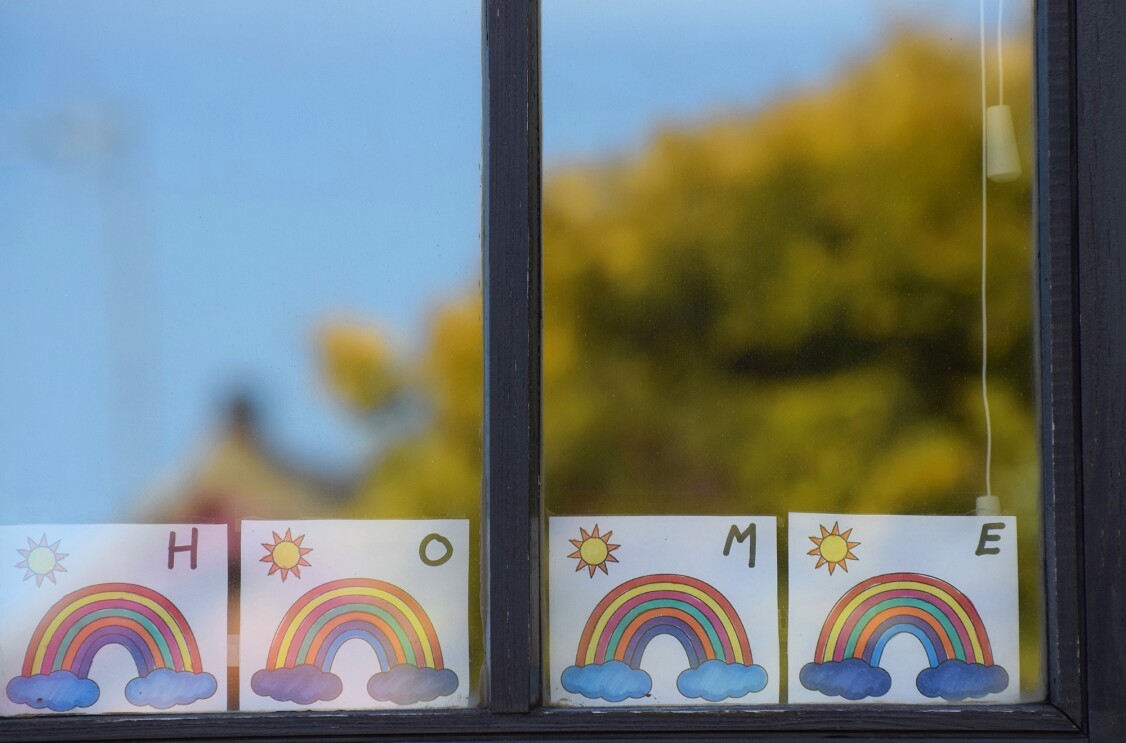 A child placing homemade rainbows in the window of their home, during COVID-19 pandemic.