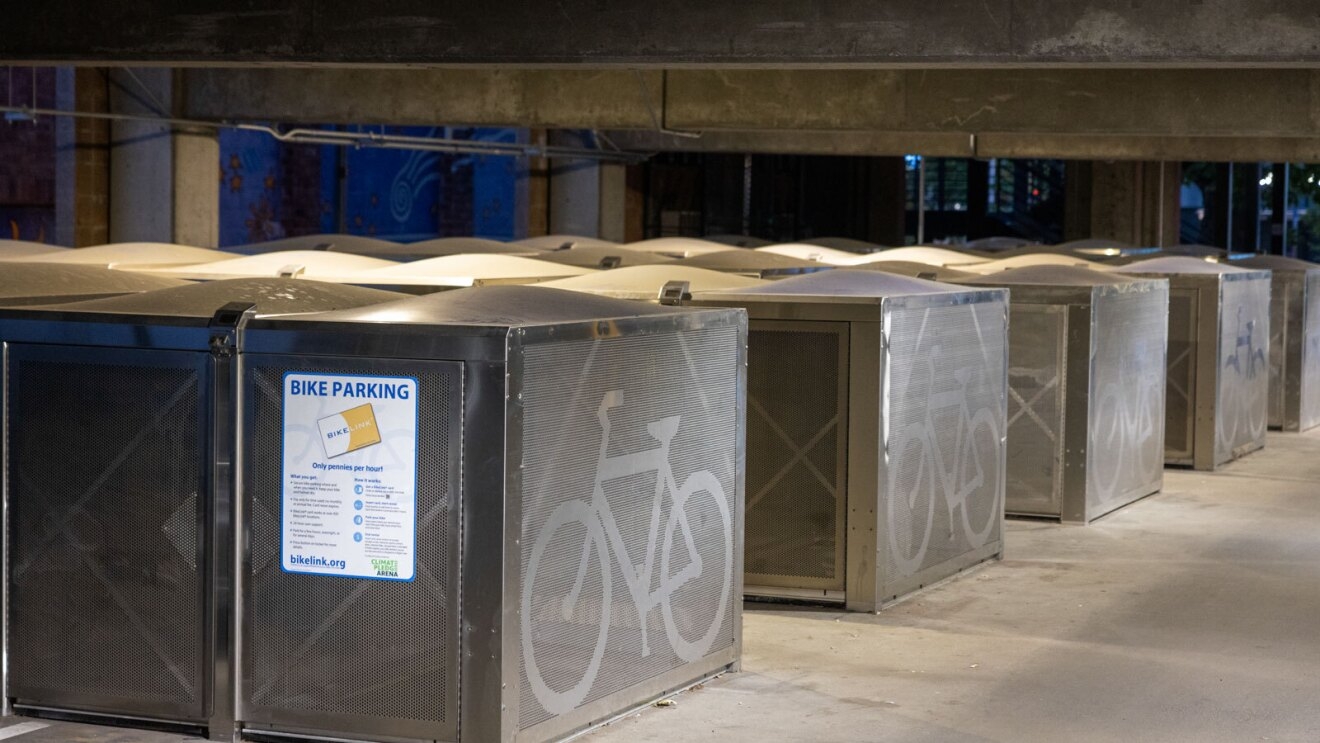 an image of several large, metal boxes with bicycle symbols painted on them. there is a sign showing that they are for bike parking.