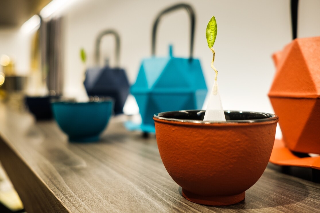 Teapots and teacups in various colors sit on a shelf.