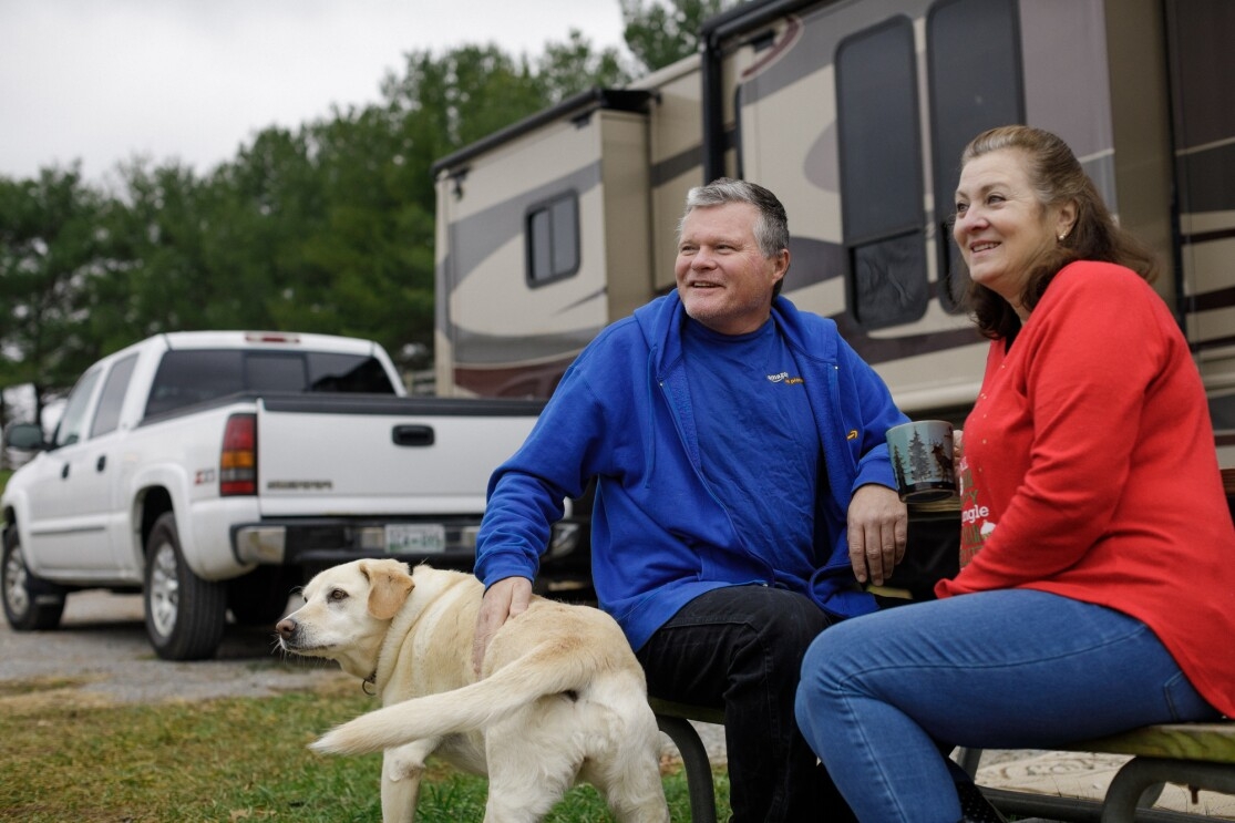 A dog, a man, and a woman photographed outside a motorhome.