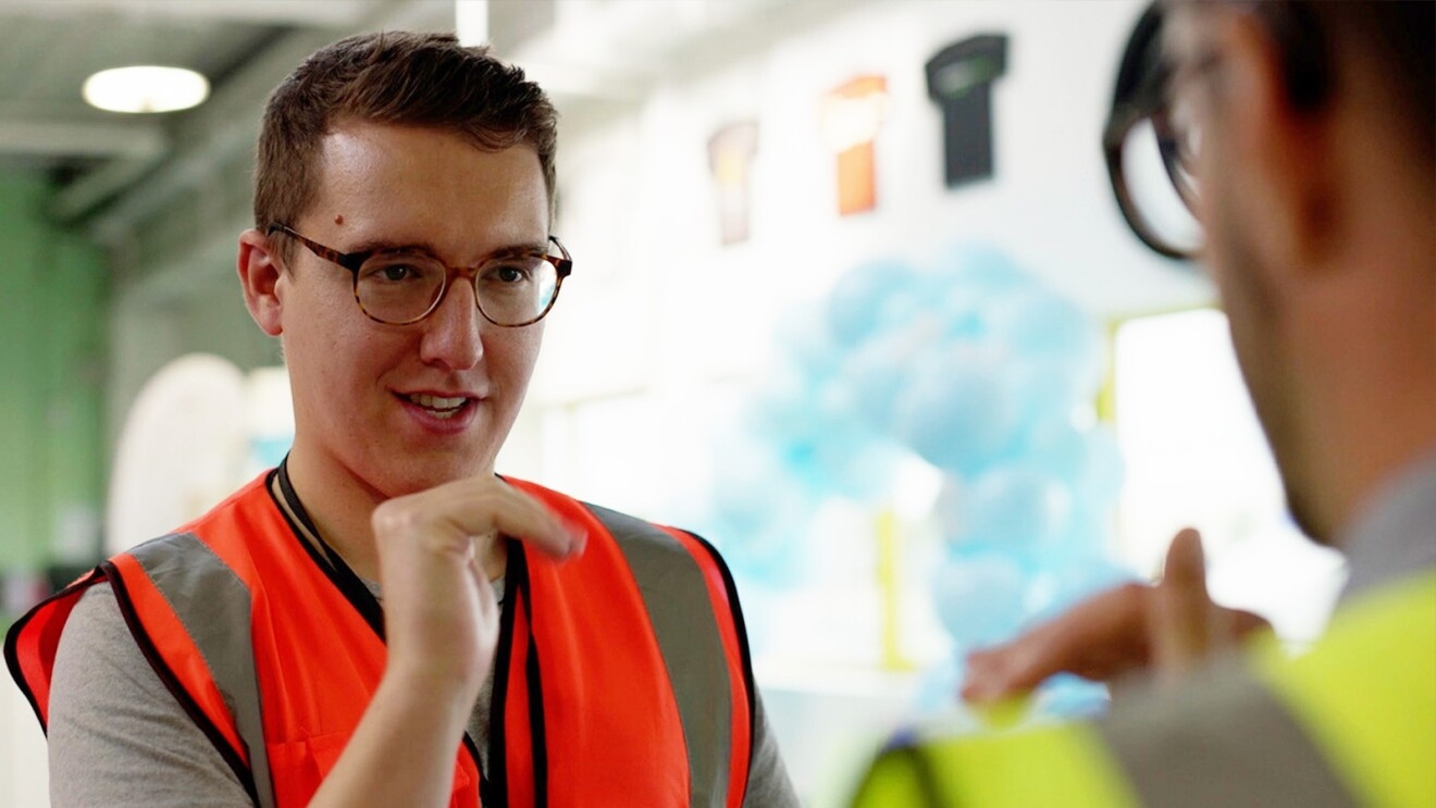 A photo of two employees at an operations center wearing safety vests, communicating with sign language.