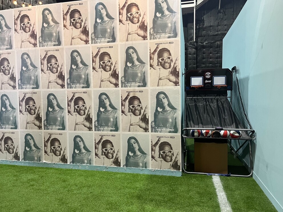 An image of a room with green, football field inspired floors and blue and white walls that show photos of Anitta and 2 Chains on the wallpaper.