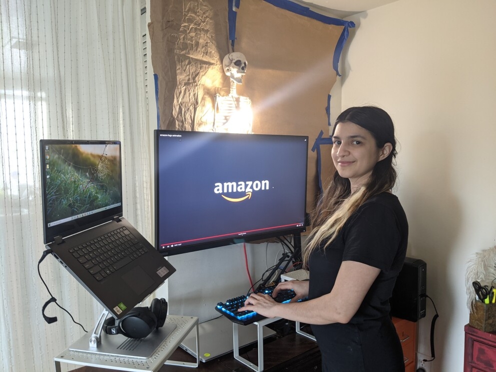 An image of an Amazon intern sitting at her computer at home, smiling for a photo with the Amazon logo on her screen in the background. 