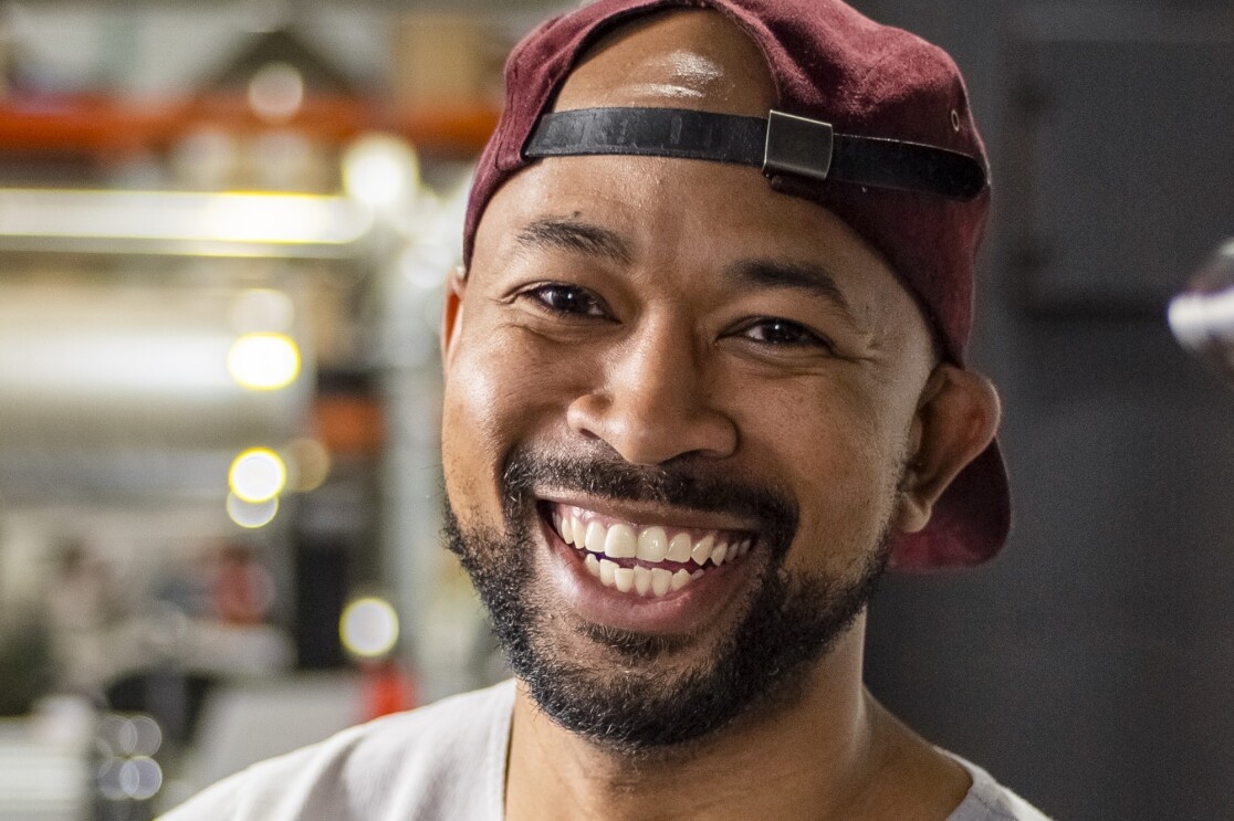 A smiling bearded man in a backwards baseball cap.