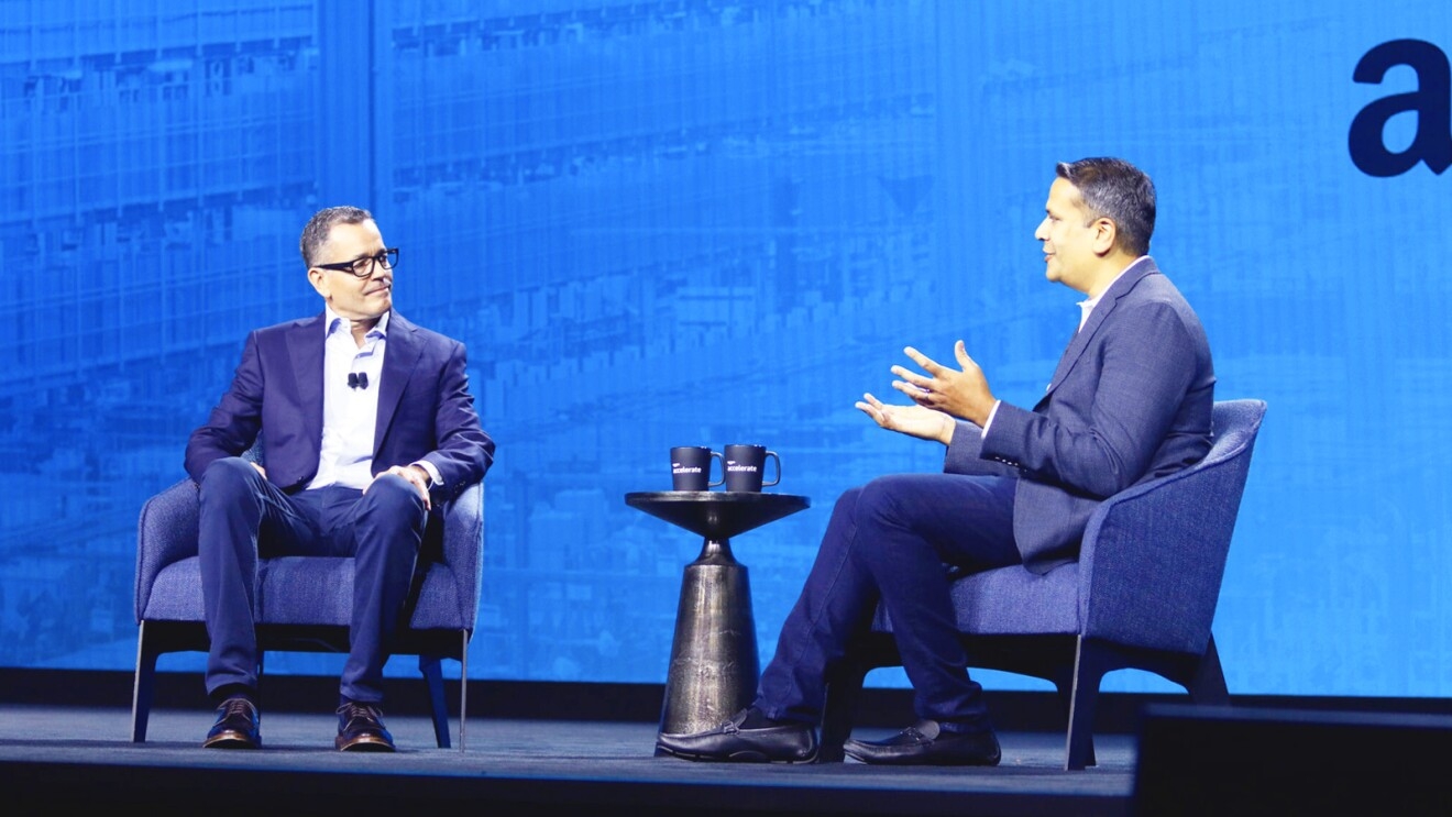 Two men sit on a conference stage talking