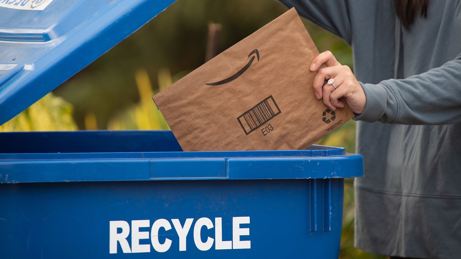 An image of a person putting an Amazon package in the recycle bin.
